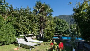 Zona de piscina con sillones de descanso, una palmera y una montaña al fondo.