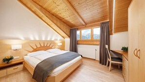 A bedroom with a bed, bedside table, lamp, window, curtains, desk, chair, and a view of the mountains. - Apartment 'Stöckerhof  Sonne' with Mountain View, Shared Pool and Wi-Fi (Merano)