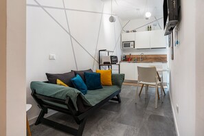 A compact living space with a sofa, a dining table, a kitchen area, and a TV mounted on the wall.