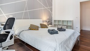 Een moderne slaapkamer met een bed, een stoel, een bureau en een nachtkastje.