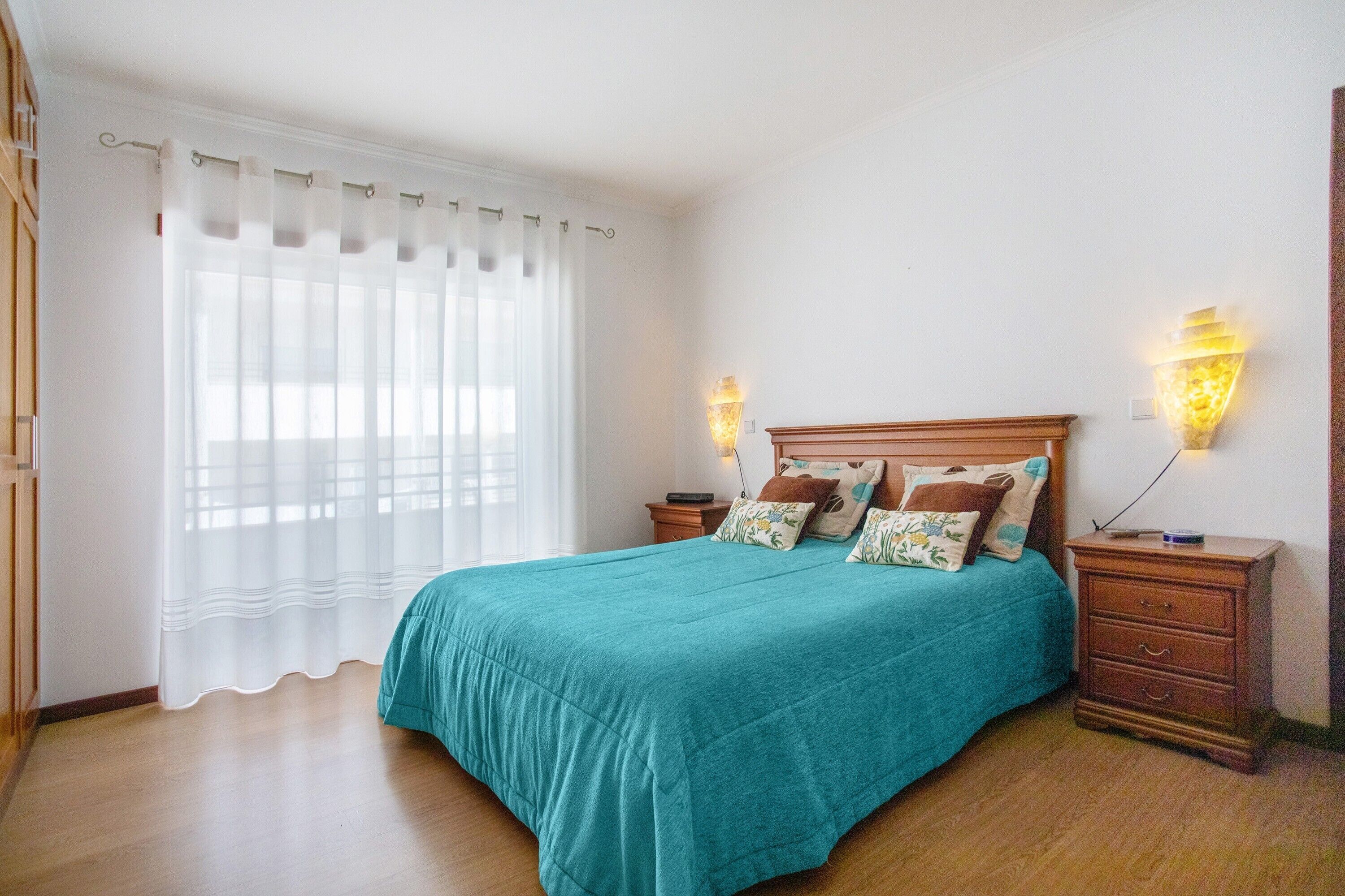 Quarto com cama, cortinas, abajures e mesa de cabeceira.
