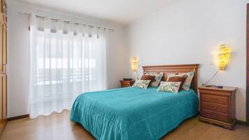 Quarto com cama, cortinas, abajures e mesa de cabeceira.