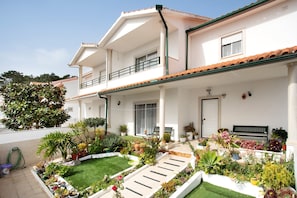 A two-story house with a balcony, a garden with various plants, and a bench. - Holiday Home 'Casa Da Cândida' with Mountain View, Private Terrace and Wi-Fi (Nazaré)