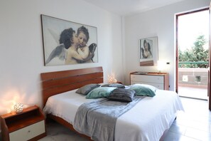 A bedroom with a bed, nightstands, a lamp, a painting, and a balcony view.