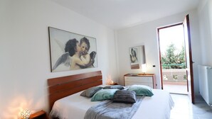 Une chambre à coucher avec un lit, des tables de chevet, une commode, un tableau et une vue sur l’ext érieur par une porte ouverte.