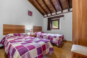 Un dormitorio con dos camas, cabeceros de madera, una mesita de noche con lámpara, una ventana con vistas a zonas verdes y techo de madera.