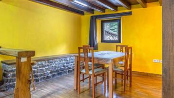A dining area with a wooden table and chairs, a stone wall, and a window with a view of trees.