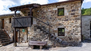 Ein Steinhaus mit einem hölzernen Balkon, einer Bank und einem kleinen Fenster.