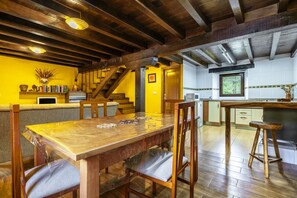 Un comedor con una mesa y sillas de madera, una cocina con armarios blancos, y una escalera que sube a un nivel superior.