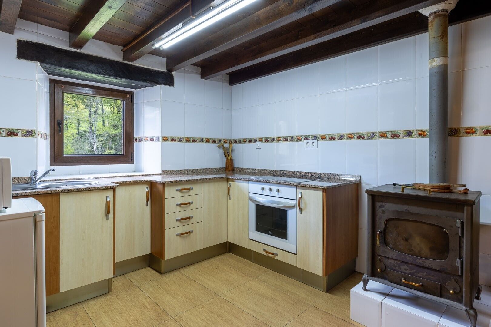 Een keuken met houten kastjes, een witte oven en een raam met uitzicht op bomen.