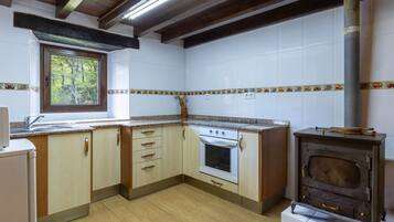 Een keuken met houten kastjes, een witte oven en een raam met uitzicht op bomen.