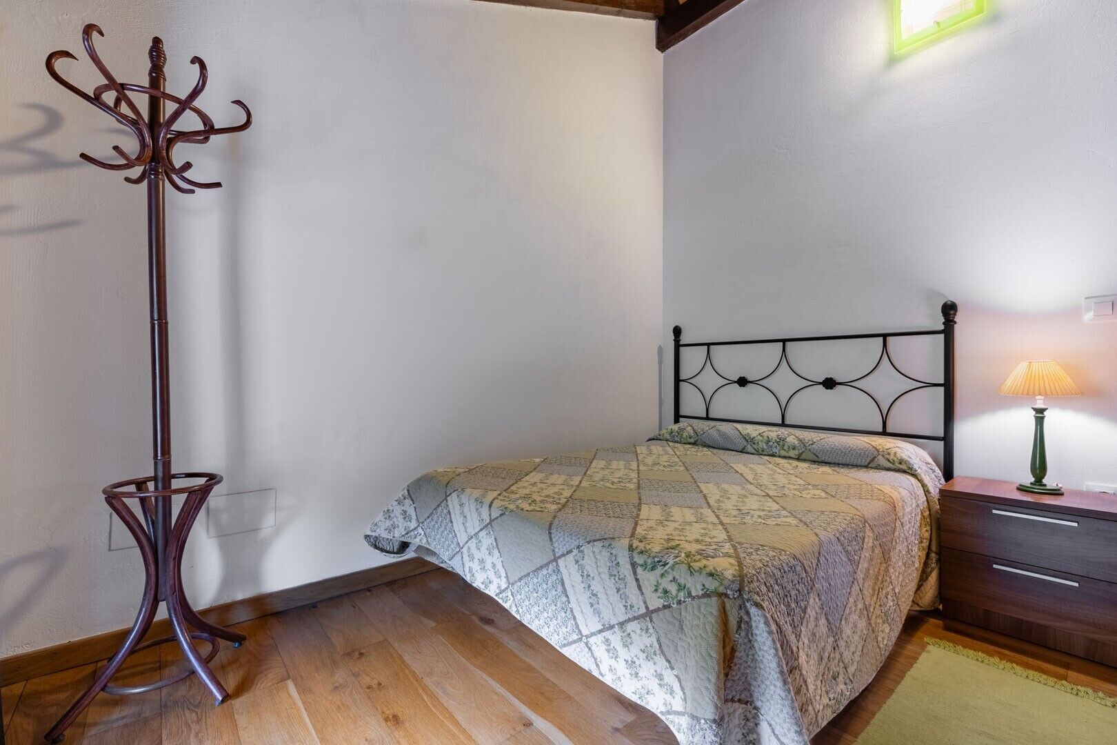 Un dormitorio con cama, mesita de noche, lámpara y lámpara de pie sobre piso de madera.