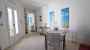 A dining area with a white table and chairs, a red rug, and a shelf with decorative items.
