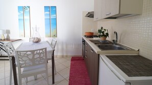 A kitchen with a dining table, chairs, a red rug, a sink, cabinets, and a window with a view.