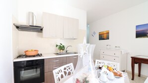A modern kitchen with a gas stove, oven, and white cabinets. There is a dining table with chairs, a vase with seashells, and a painting on the wall.