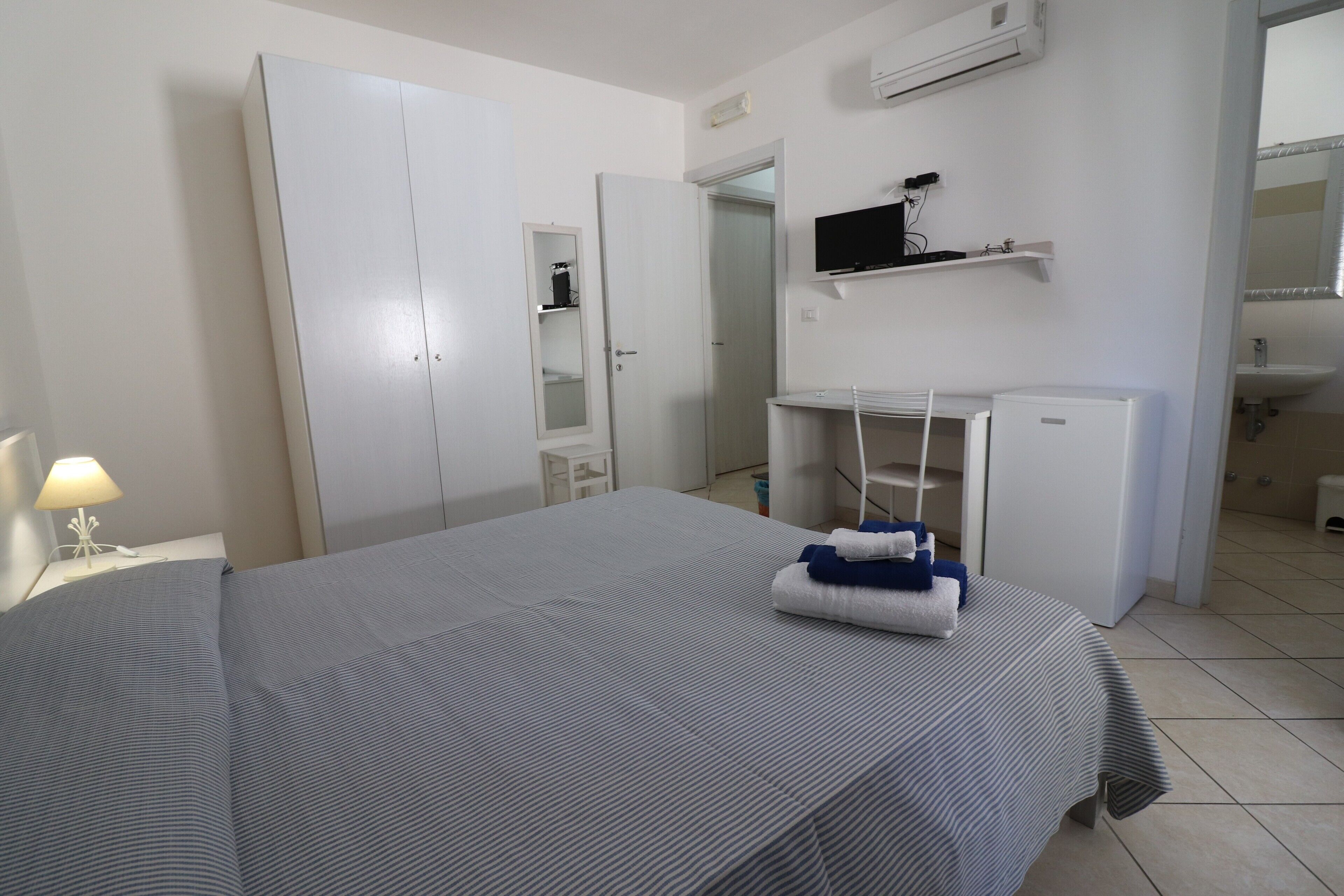 A hotel room with a bed, wardrobe, desk, and a television on a shelf.