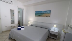 A hotel room with a bed, bedside tables, a mirror, a painting of a beach, and a refrigerator.