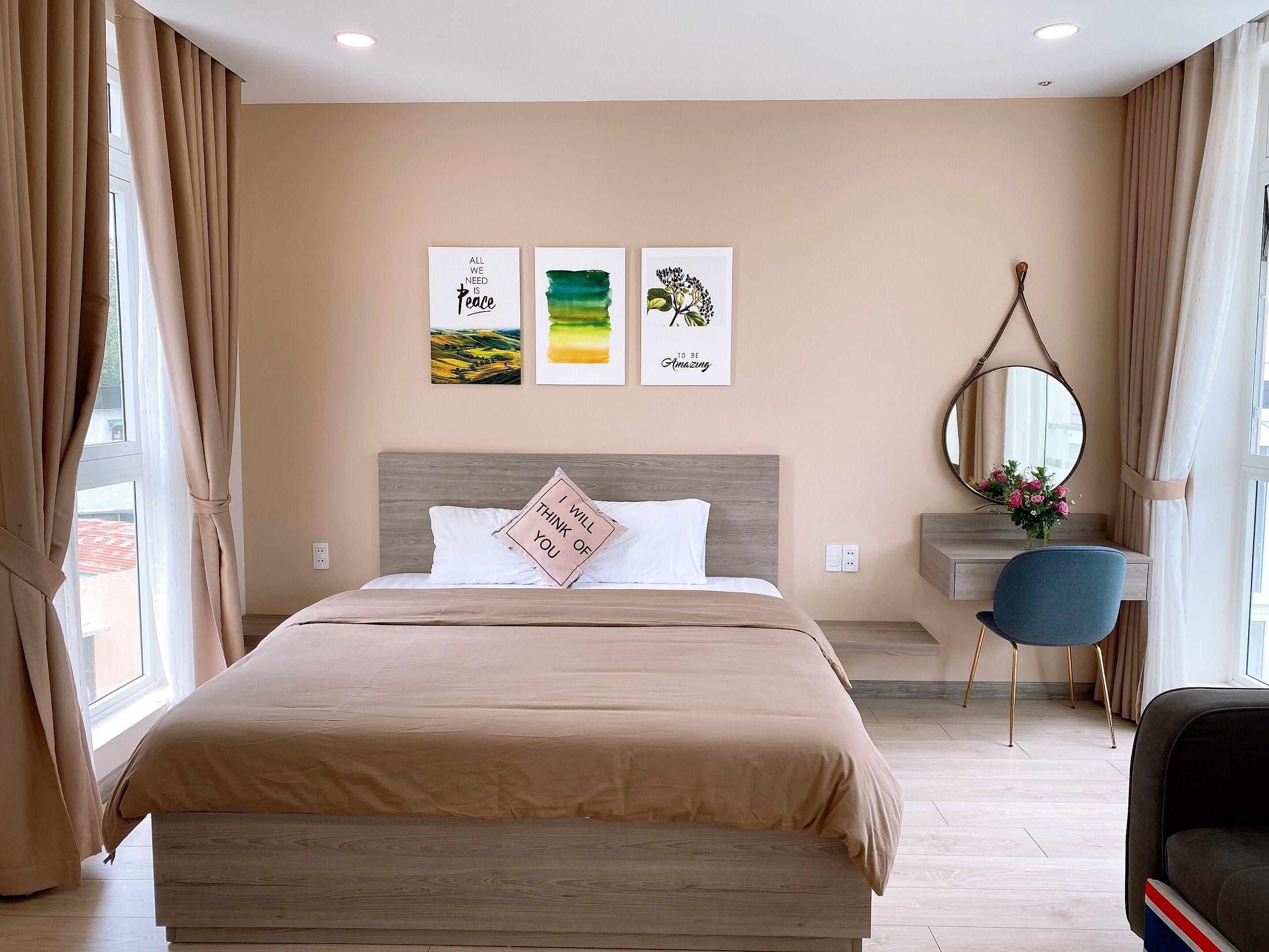 A hotel room with a large bed, a bedside table with a mirror, and a chair. There are three wall art pieces above the bed.