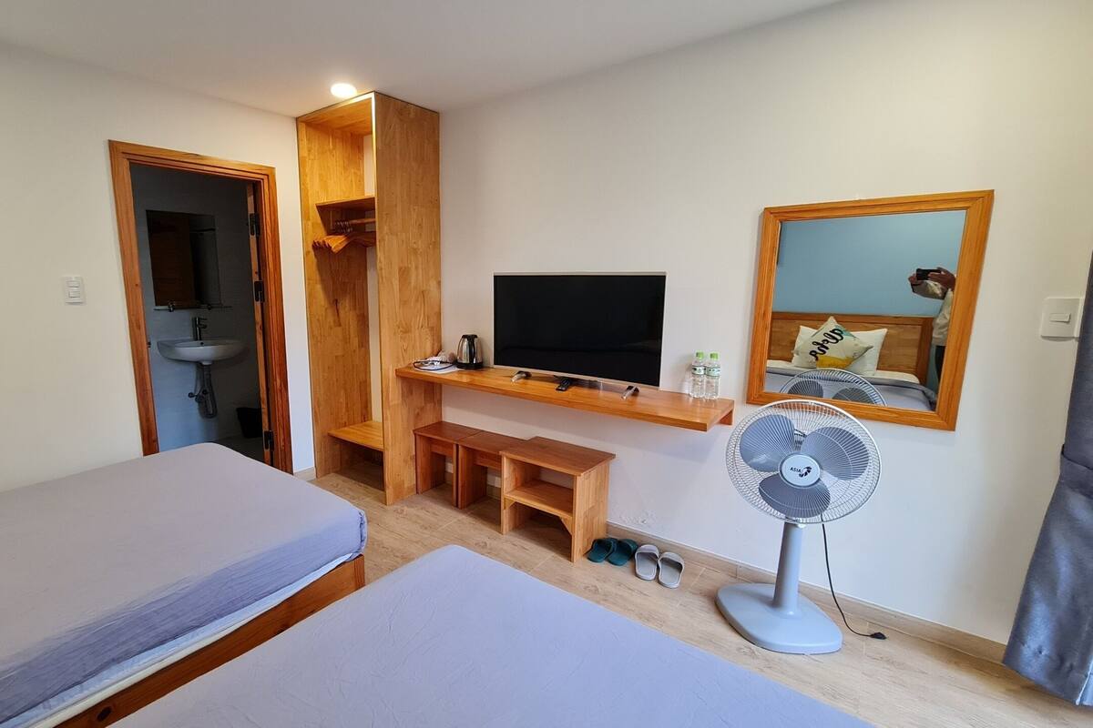 A compact room with two single beds, a wooden desk with a TV, a small sink, and a mirror.