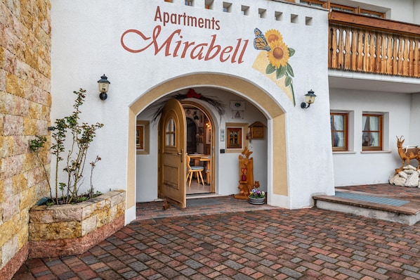 A building with a sign reading 'Apartments Mirabell,' an entrance with a wooden door, and a brick-paved courtyard.