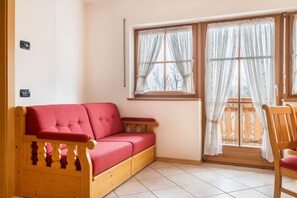 A room with a red sofa, a wooden chair, a window with curtains, and a tiled floor.