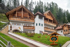Un edificio de estilo chalet de madera con balcones, un letrero que dice 'Apartments Mirabell' y un paisaje montañoso circundante.