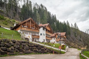 A wooden chalet with balconies, a stone wall, and a mountain backdrop.