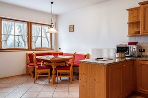 Keittiössä on puukehikoiset kaapit, ruokapöytä tuoleineen, sisäänrakennettu uuni ja ikkuna, jossa on verhot.