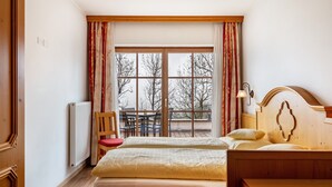 Une chambre d’hôtel avec deux lits, un radiateur, une chaise, une table et un balcon donnant sur des arbres.