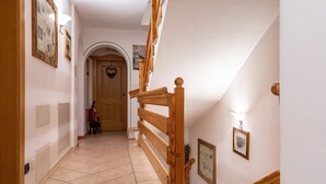 Un couloir avec un escalier en bois, une porte ornée d’un motif en forme de cœur et des tableaux encadrés accrochés aux murs.