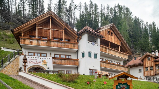 Un bâtiment de style chalet en bois, doté de balcons, sur lequel on peut lire l’inscription « Appartements Mirabell », et entouré d’un paysage montagneux.