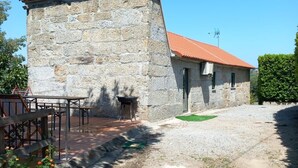A stone building with a red-tiled roof, outdoor seating, and a gravel path.