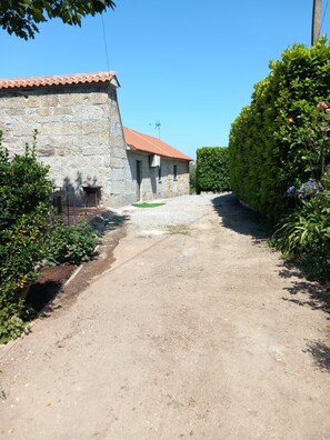 Un edificio de piedra con techo de tejas rojas, un camino de grava y follaje circundante.