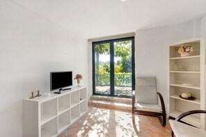 A modern living room with a television, a white console table, a chair, and a large window with a view of greenery.