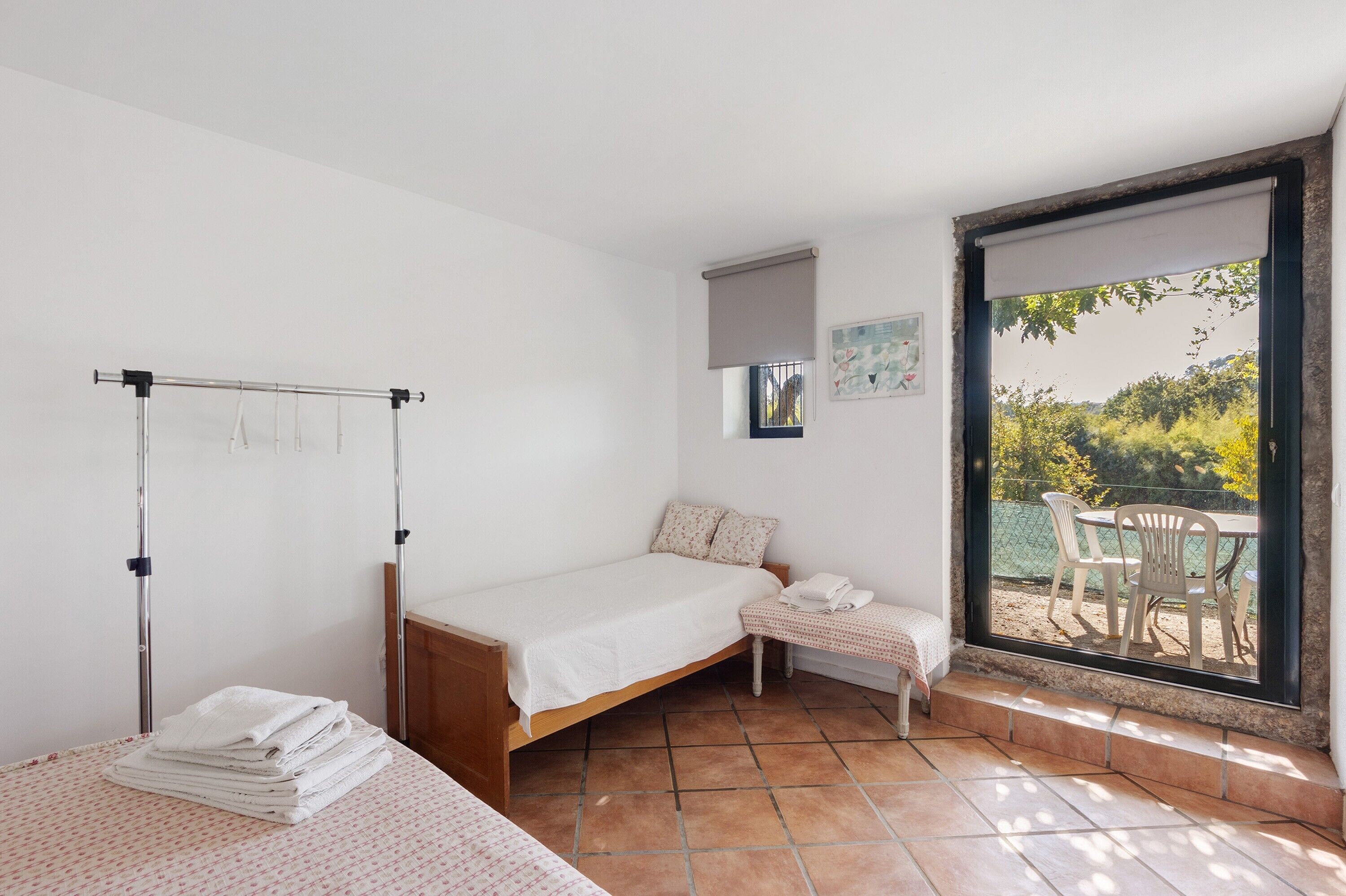 A bedroom with a bed, a small table with a chair, a window with a view, and a balcony.