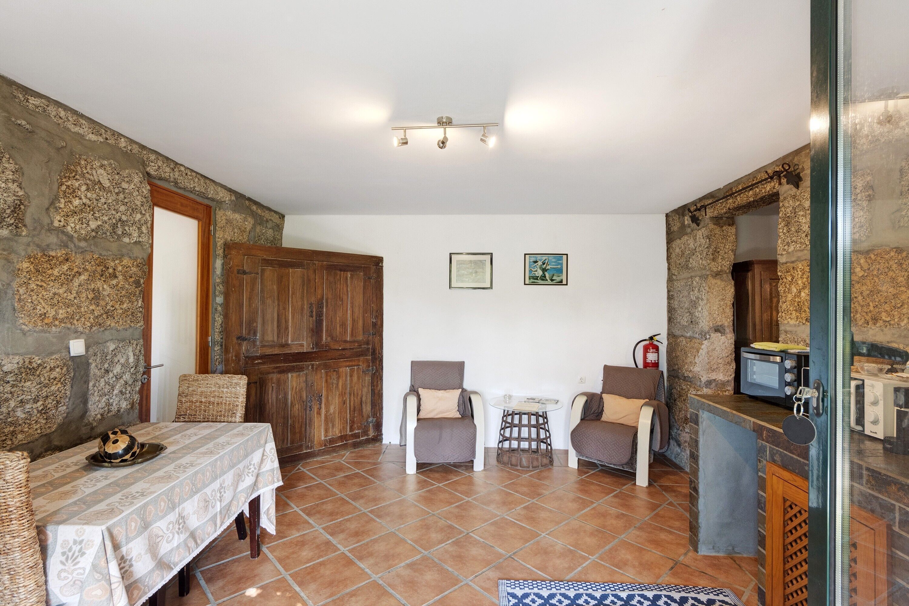 A dining area with a table, chairs, a small round table, and a stone wall.