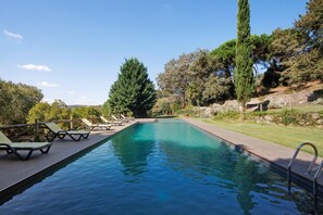 Una piscina con lettini, circondata da alberi e un muro in pietra.