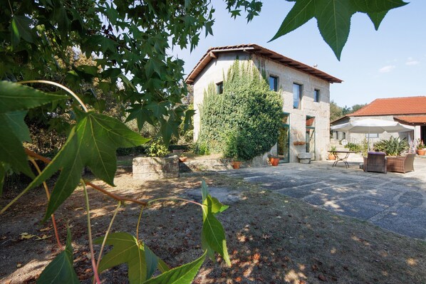 Un bâtiment en pierre avec un toit en tuiles, entouré d’une cour pavée aménagée avec du mobilier d’extérieur et des plantes en pot.