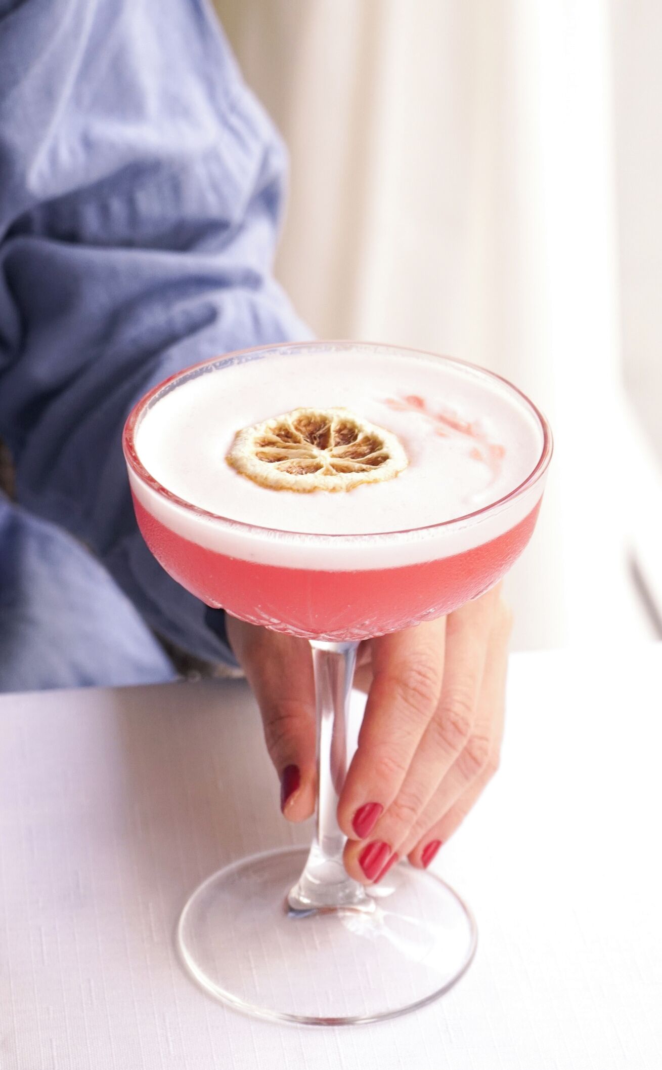 Ein Cocktail im Glas mit Garnitur, gehalten von einer Person mit rotem Nagellack.