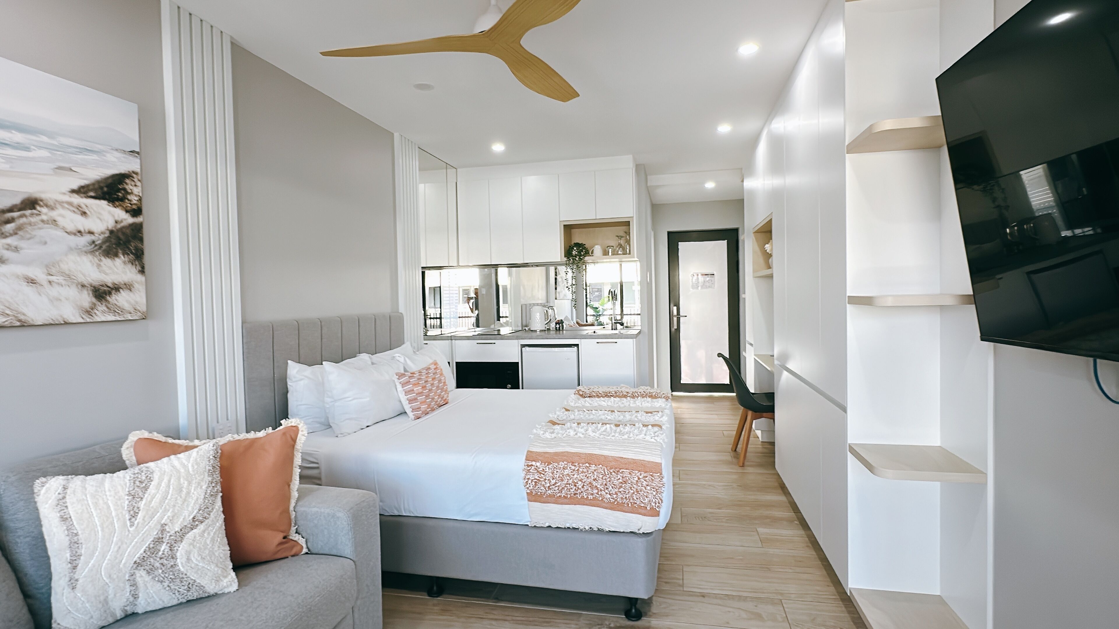 Una habitación de hotel moderna con cama, sofá, televisor y kitchenette.