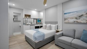 Une chambre moderne avec un lit, un canapé gris, une télévision et un coin cuisine.