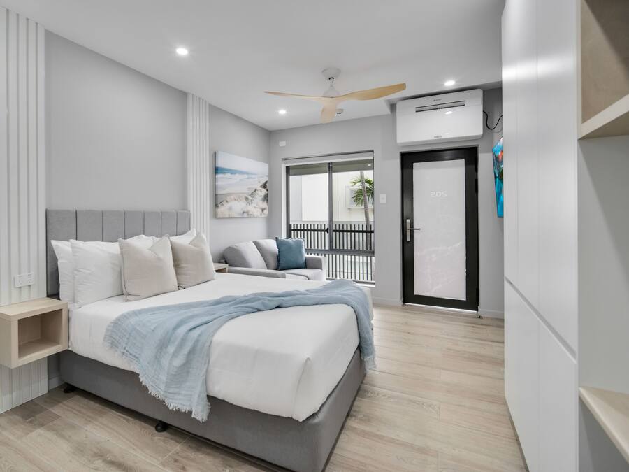 A modern bedroom with a bed, bedside tables, a ceiling fan, and a window with a view.