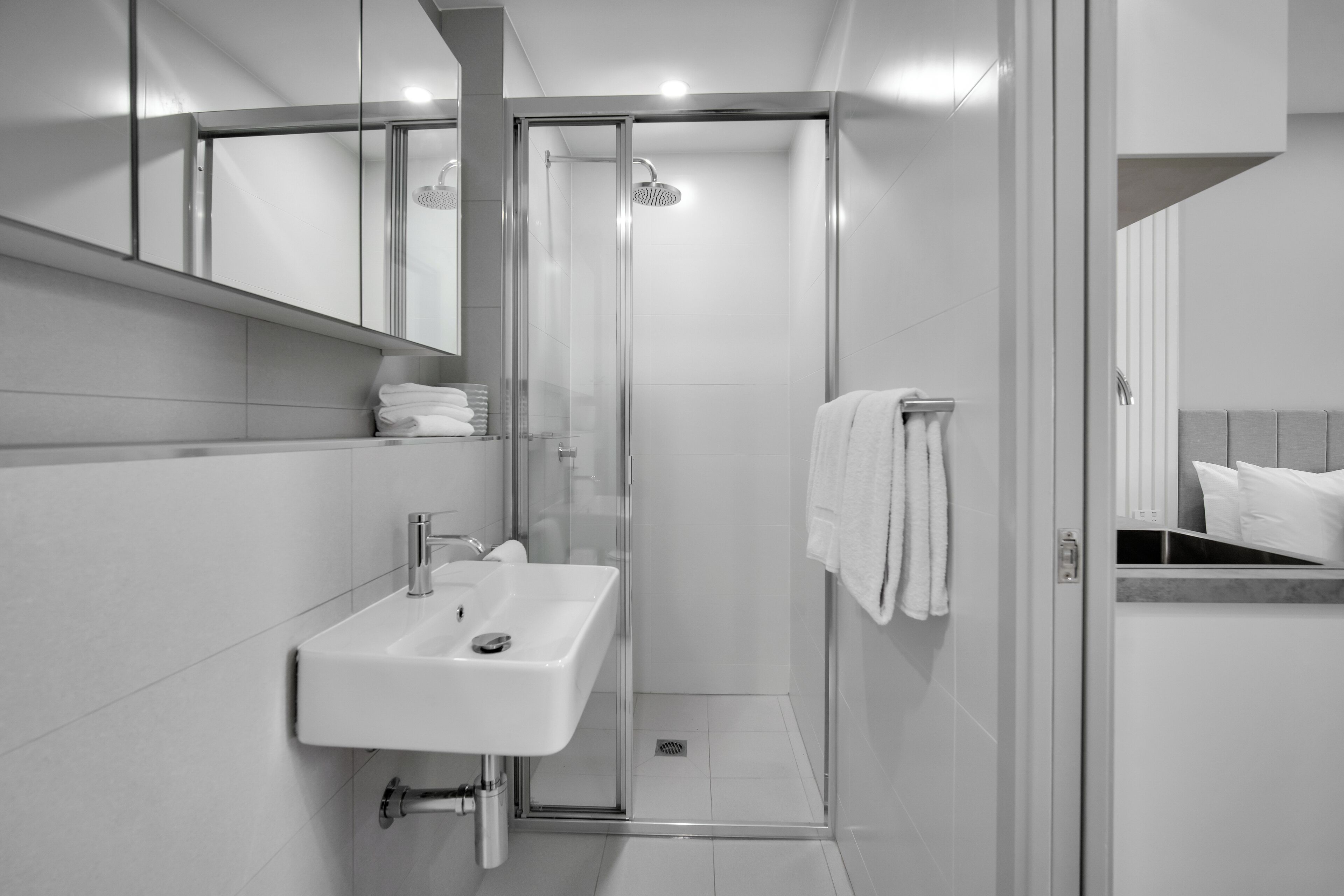 A modern bathroom with a glass-enclosed shower, a white sink, and a towel rack.