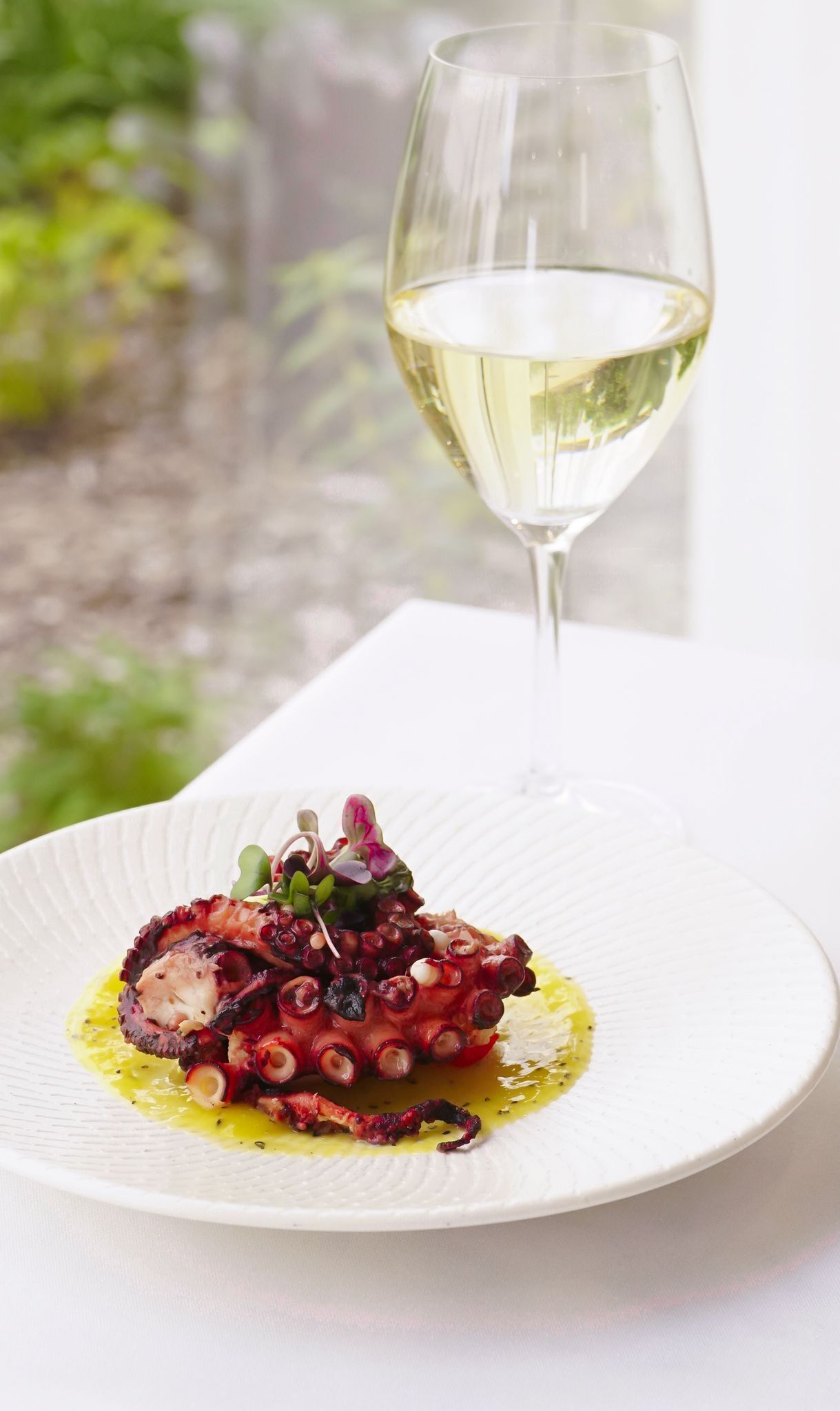Un plato de pulpo con una copa de vino blanco sobre una mesa.
