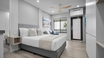 Quarto moderno com uma cama grande, mesas de cabeceira, ventilador de teto, ar condicionado e uma porta de vidro deslizante para uma varanda.