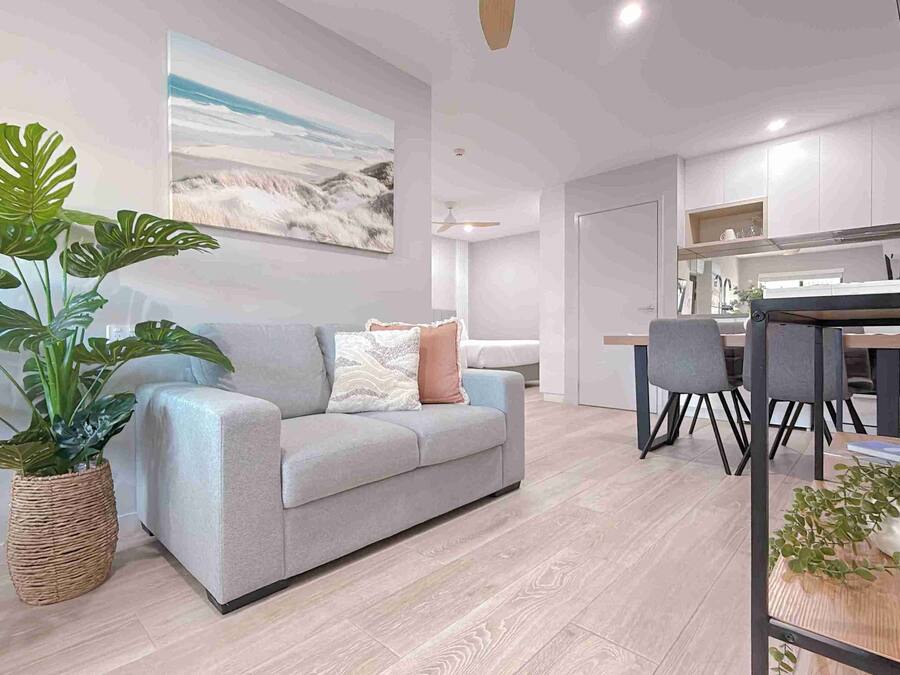 Un salon moderne avec un canapé gris, une grande plante en pot et un coin repas comprenant une table et des chaises.