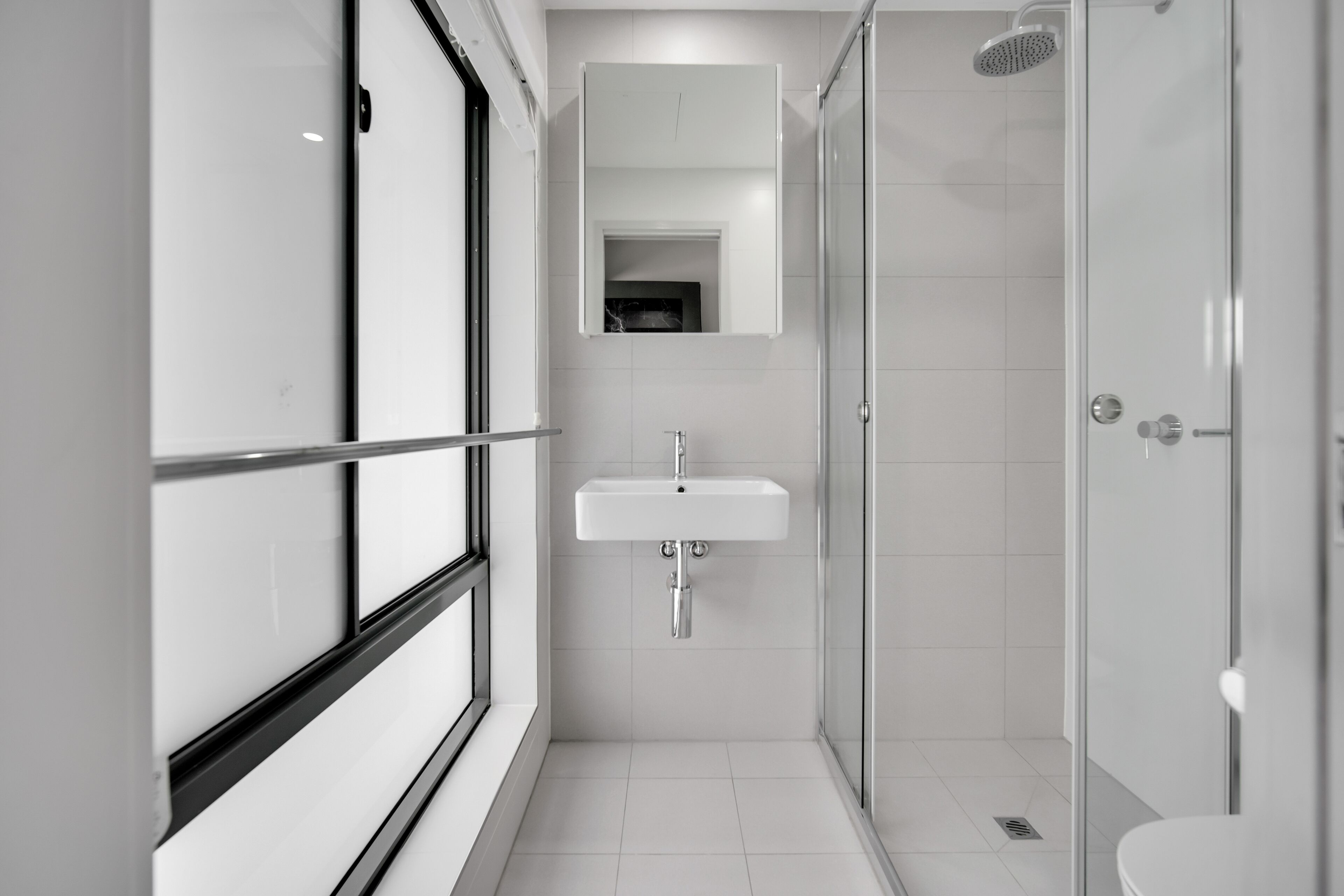 A modern bathroom with a glass shower enclosure, a white sink, and a large mirror above the sink.