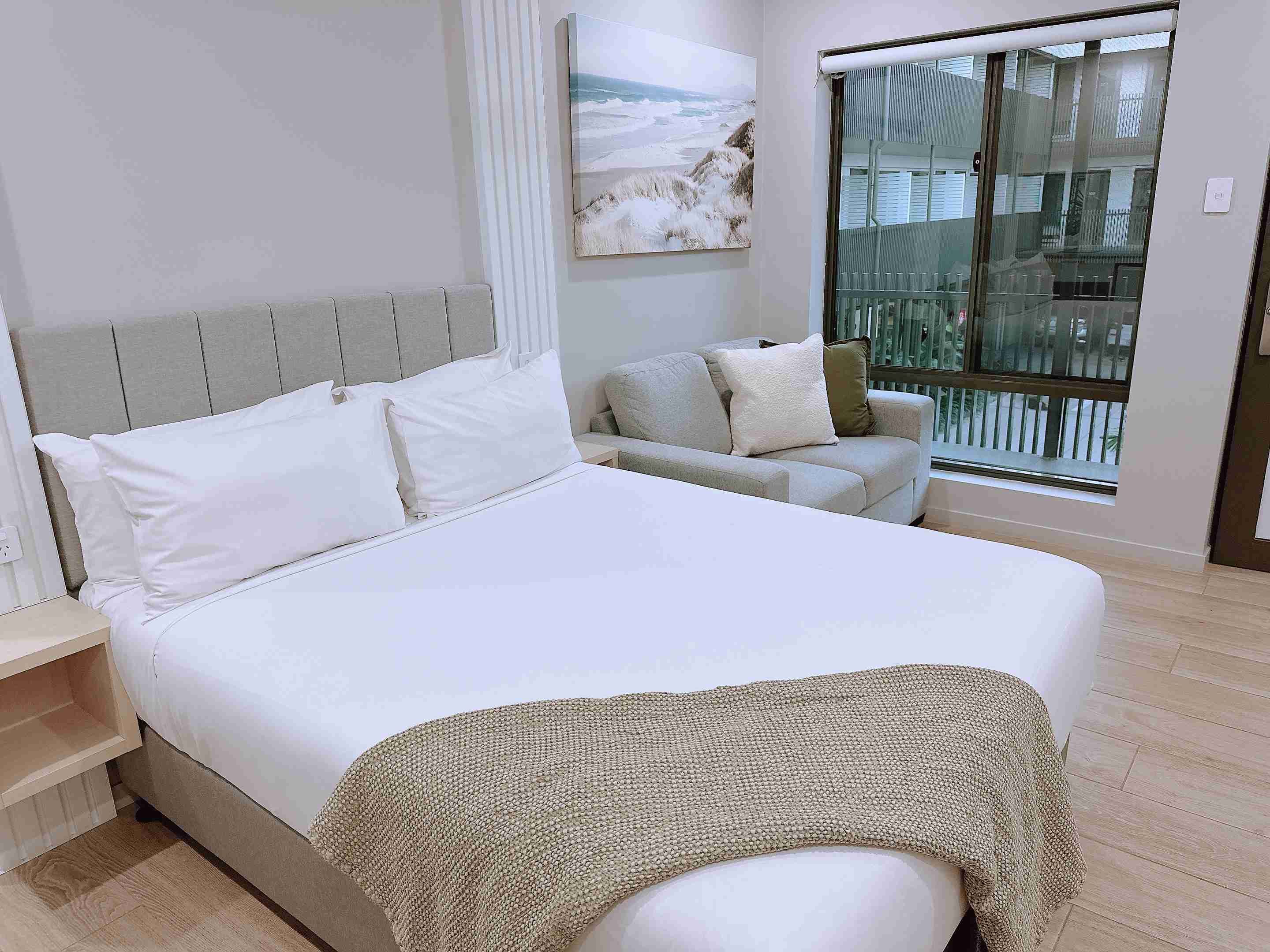 Een slaapkamer met een bed, een bank, een raam met uitzicht op een balkon en een schilderij aan de wand.