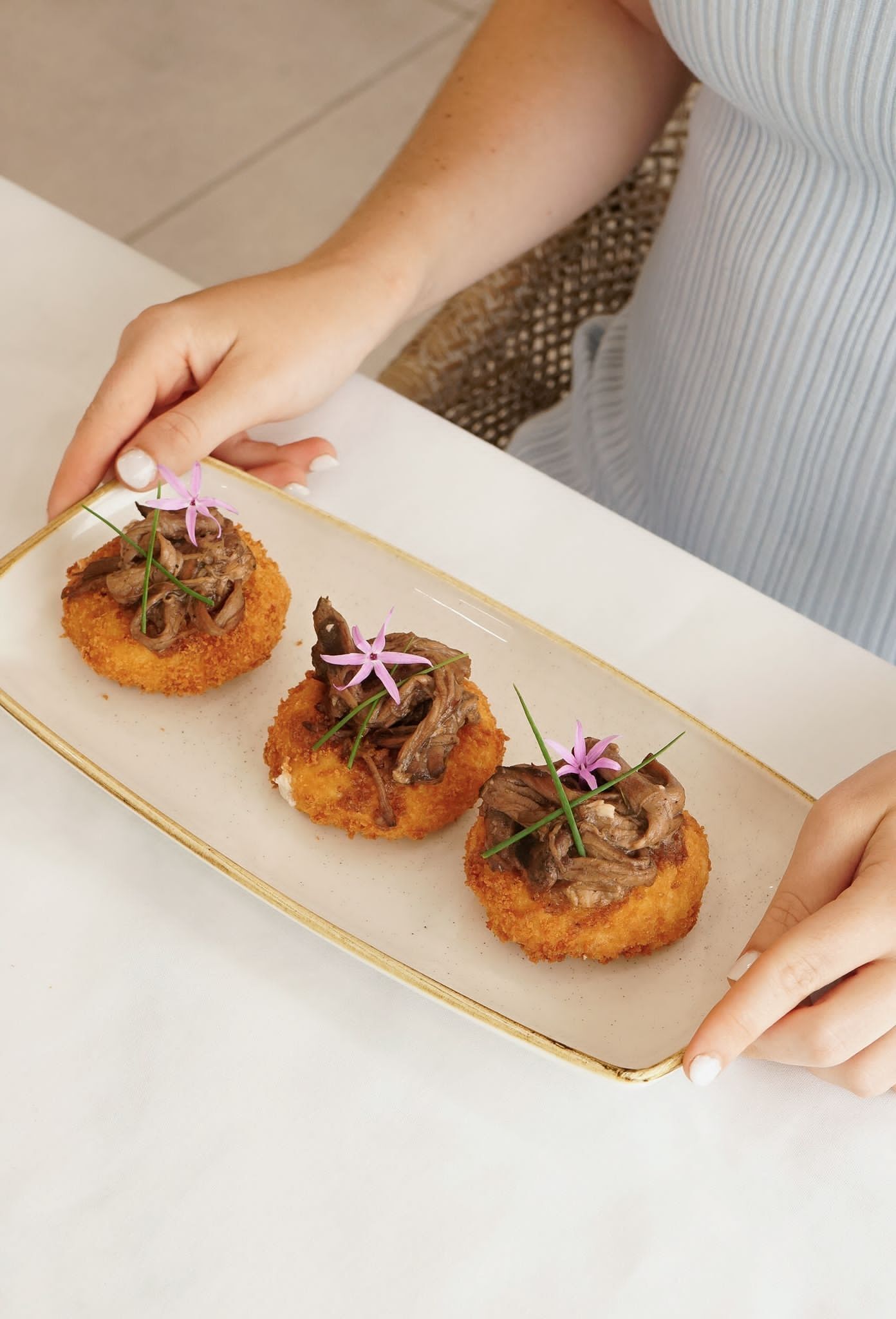 A person holding a rectangular plate with three food items, each topped with a flower.