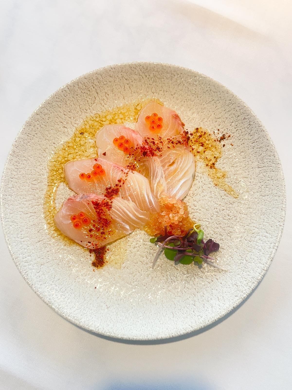 A plate of sashimi with roe and a garnish of greens.